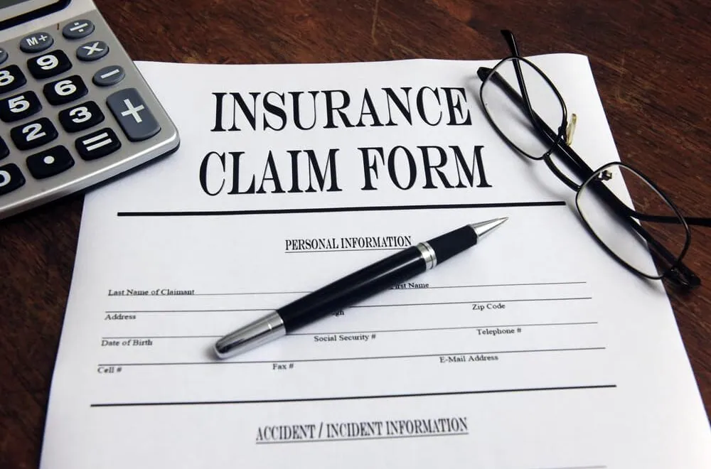 Blank insurance claim form on a desk with a pen, reading glasses, and a calculator